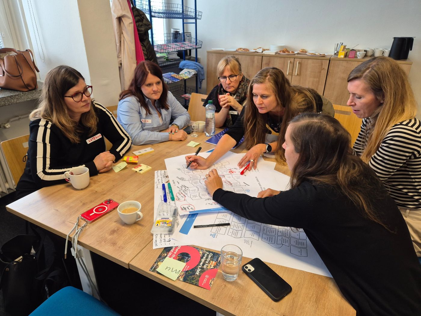 Facilitovaný workshop: skupina účastnic u stolu nad společnou mapou na velkém papíru